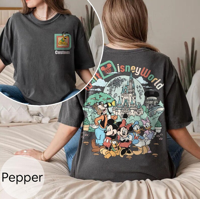 May include: Pepper-coloured t-shirt with a Disney World graphic on the back and a Pluto design on the front. The back graphic includes Mickey Mouse, Minnie Mouse, Donald Duck, and Goofy. The shirt has the text "Custom" on the front.