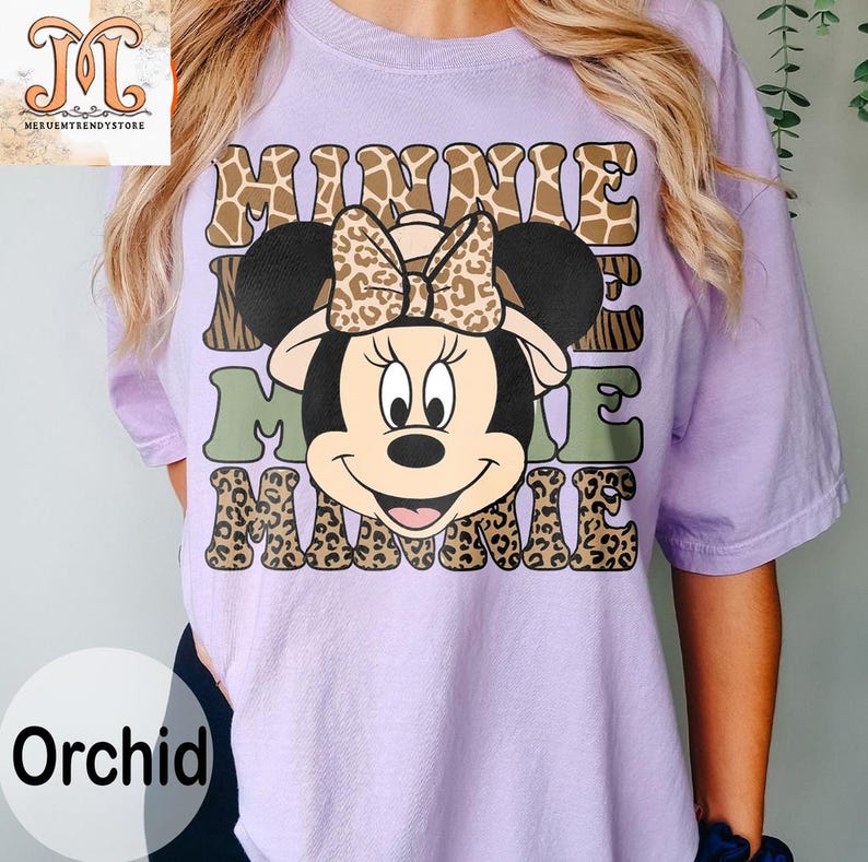 May include: A purple t-shirt with a graphic of Minnie Mouse wearing a safari hat. The graphic is surrounded by the word "Minnie" in a leopard print pattern.