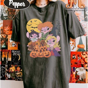 May include: Dark gray Comfort Colors Pepper t-shirt featuring a Halloween-themed graphic. The graphic includes cartoon characters, jack-o'-lanterns, a full moon, and bats. The shirt has the text "Comfort Colors" and "Pepper" in an oval.