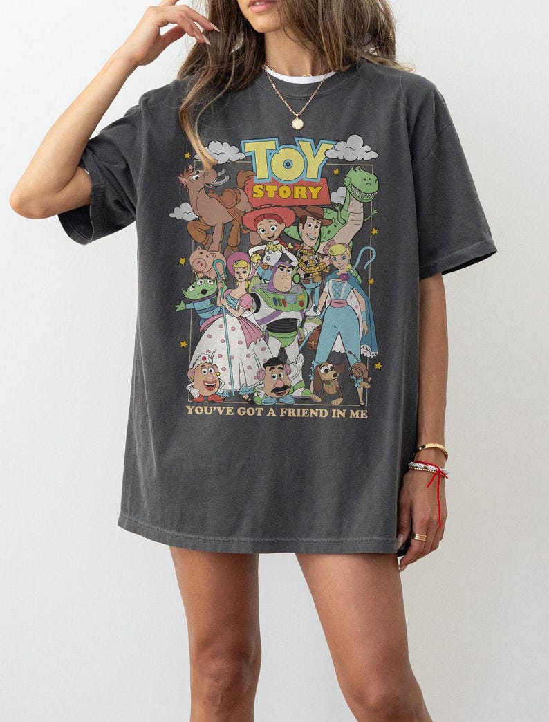 Puede incluir: Camiseta gris oscuro con un gr&aacute;fico colorido de los personajes de Toy Story. El dise&ntilde;o incluye el t&iacute;tulo de la pel&iacute;cula y la frase "You've Got a Friend in Me". La camiseta tiene un aspecto vintage, ligeramente descolorido.