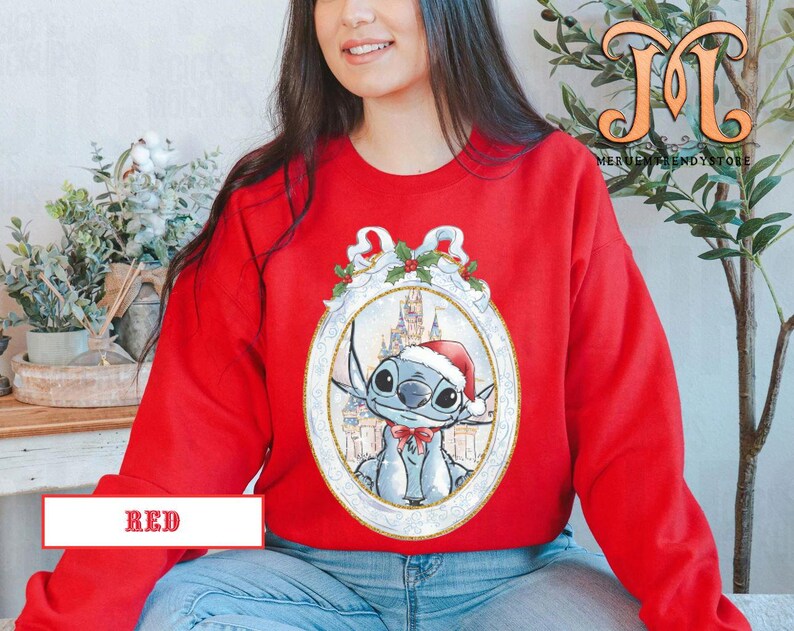 May include: A red sweatshirt featuring a cartoon character in a Santa hat and a bow tie, set within an ornate frame. The frame includes a castle and holly accents. The word "RED" is displayed in a white box at the bottom.