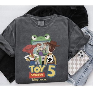 May include: A charcoal gray long-sleeve shirt featuring a graphic from the movie Toy Story 5. The graphic includes characters Woody, Buzz Lightyear, Jessie, and others. The shirt also has the Disney Pixar logo.