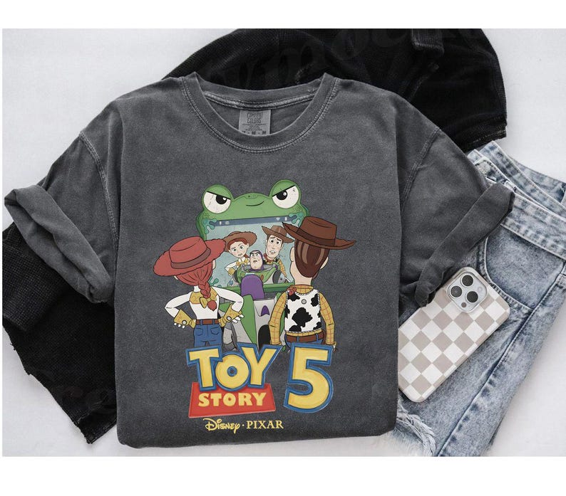 May include: A charcoal gray long-sleeve shirt featuring a graphic from the movie Toy Story 5. The graphic includes characters Woody, Buzz Lightyear, Jessie, and others. The shirt also has the Disney Pixar logo.