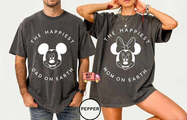 May include: Two charcoal gray t-shirts with white graphic designs. One shirt features Mickey Mouse with the text "THE HAPPIEST DAD ON EARTH." The other shirt features Minnie Mouse with the text "THE HAPPIEST MOM ON EARTH."