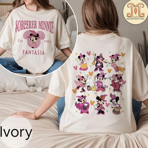 May include: A white t-shirt with a pink graphic of Minnie Mouse as a sorceress. The text "Sorcerer Minnie" is printed above the graphic and "Est. 1940 Fantasia" is printed below the graphic. The back of the shirt features a pink graphic of nine Minnie Mouse sorceresses in different poses.
