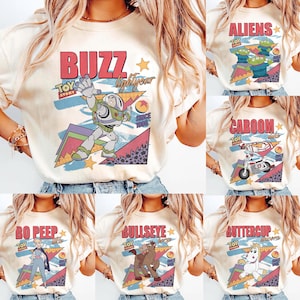 May include: Cream-colored t-shirts featuring various Toy Story characters and phrases. Designs include "Buzz Lightyear," "Aliens," "Caboom," "Bo Peep," "Bullseye," and "Buttercup," with retro-style graphics and the Toy Story logo.