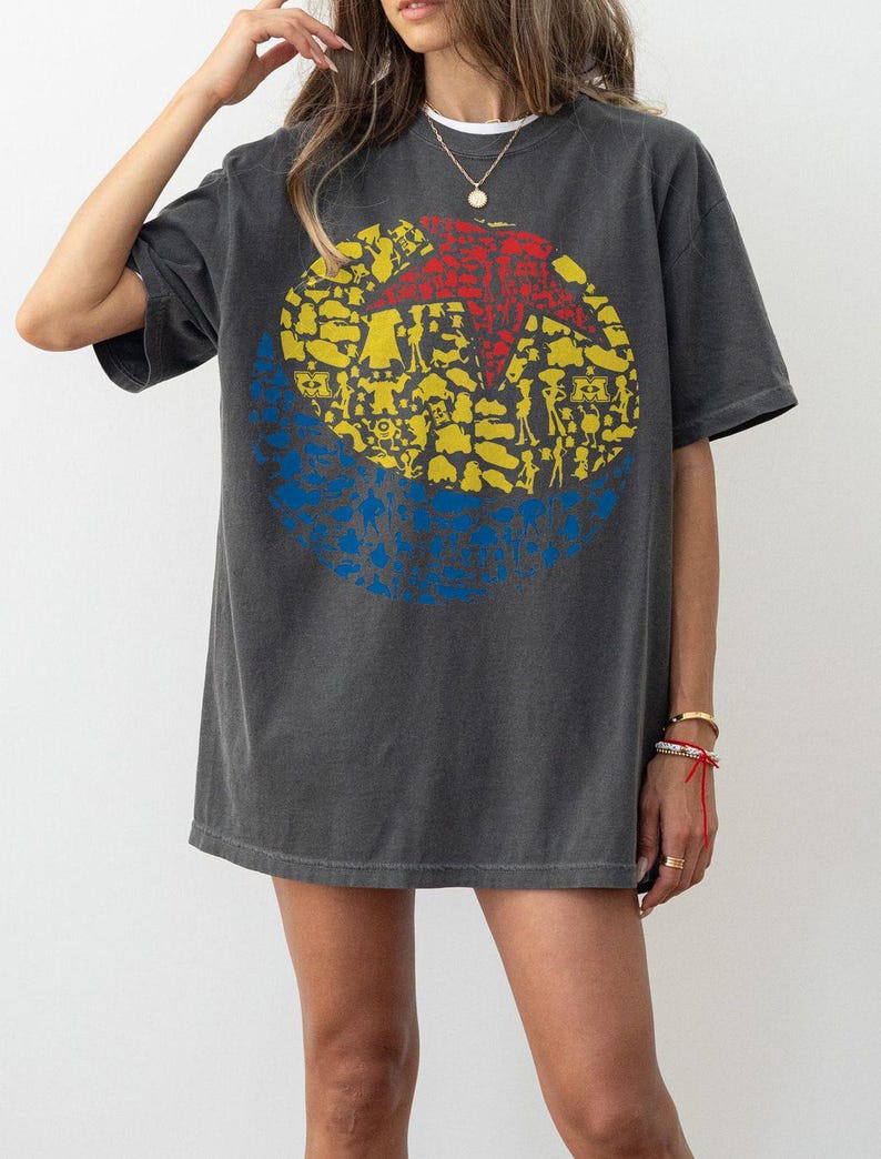 May include: Dark gray t-shirt featuring a large graphic of a red star inside a yellow circle, with blue accents. The graphic is filled with various shapes and figures. The shirt has short sleeves and a relaxed fit.