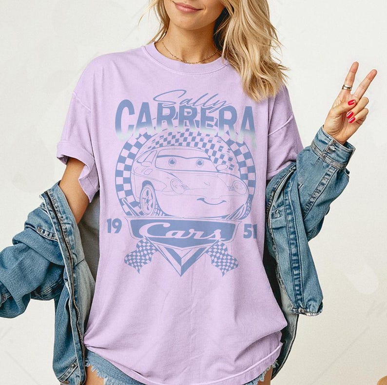May include: A light purple t-shirt featuring a graphic of the character Sally Carrera from the movie Cars. The design includes the text "Sally Carrera" above an image of the car, with "Cars" and the numbers "19" and "51" below.