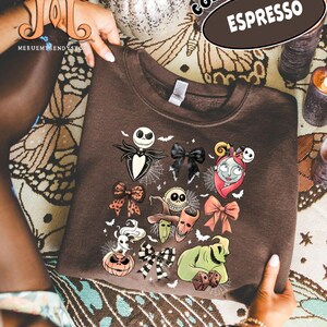 Puede incluir: Sudadera marr&oacute;n oscuro con un dise&ntilde;o de personajes de Pesadilla antes de Navidad. El dise&ntilde;o incluye a Jack Skellington, Sally y otros personajes. La sudadera tiene las palabras "Comfort Colors" y "Espresso" impresas.