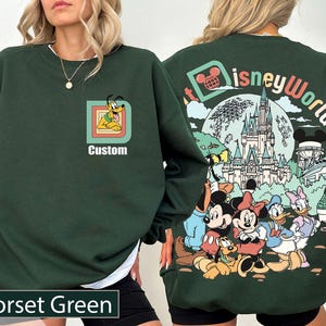 May include: Dark green sweatshirt featuring a Pluto graphic and the word "Custom". The back displays a Disney World design with Mickey, Minnie, Donald, and Daisy Duck. The sweatshirt is labelled "Forset Green".