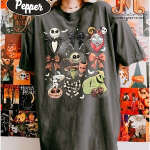 Puede incluir: Camiseta gris oscuro con varios personajes y dise&ntilde;os de lazos de "Pesadilla antes de Navidad". La camiseta incluye a Jack Skellington, Sally, Oogie Boogie y otros elementos ic&oacute;nicos. El texto "COMFORT COLORS Pepper" es visible en la parte superior.