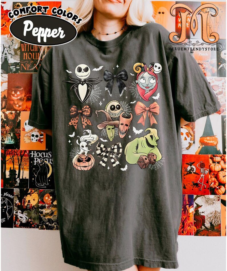 Puede incluir: Camiseta gris oscuro con varios personajes y dise&ntilde;os de lazos de "Pesadilla antes de Navidad". La camiseta incluye a Jack Skellington, Sally, Oogie Boogie y otros elementos ic&oacute;nicos. El texto "COMFORT COLORS Pepper" es visible en la parte superior.