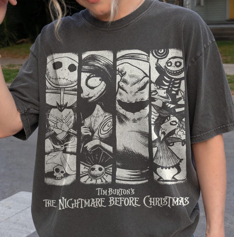 May include: A charcoal gray t-shirt featuring a graphic print of characters from Tim Burton's The Nightmare Before Christmas. The design consists of four vertical panels displaying Jack Skellington, Sally, Oogie Boogie, and other figures.