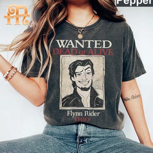 Puede incluir: Una camiseta negra con un diseño de cartel de se busca de estilo vintage con un personaje de dibujos animados con el texto "WANTED DEAD OR ALIVE" y "Flynn Rider THIEF".