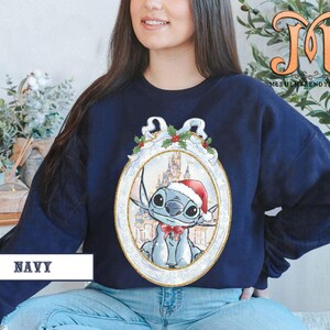 May include: Navy blue sweatshirt featuring a cartoon character wearing a Santa hat and a red bow tie, set against a castle backdrop within an ornate frame. The word "NAVY" is printed at the bottom.