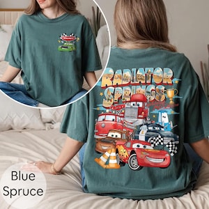 Puede incluir: Camiseta azul abeto con un gr&aacute;fico de coches de dibujos animados y el texto "Radiator Springs". La parte delantera de la camiseta tiene un peque&ntilde;o gr&aacute;fico de un coche de carreras. La parte trasera de la camiseta tiene un gr&aacute;fico m&aacute;s grande con varios coches y el texto "Radiator Springs".