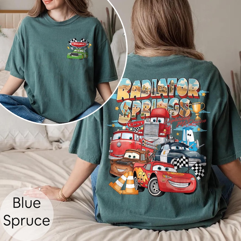 Puede incluir: Camiseta azul abeto con un gr&aacute;fico de coches de dibujos animados y el texto "Radiator Springs". La parte delantera de la camiseta tiene un peque&ntilde;o gr&aacute;fico de un coche de carreras. La parte trasera de la camiseta tiene un gr&aacute;fico m&aacute;s grande con varios coches y el texto "Radiator Springs".