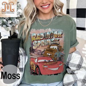 May include: A green t-shirt with a vintage-style graphic of Lightning McQueen and Mater from the movie Cars. The graphic says "Radiator Springs" in a faded, distressed font.