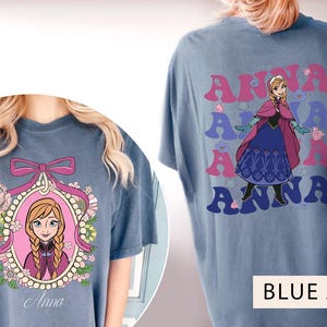 May include: Two blue jean t-shirts featuring a cartoon image of Anna from Frozen. One shirt has a single image of Anna in a pink frame with flowers. The other shirt has a repeated image of Anna with the word "Anna" in a retro font.
