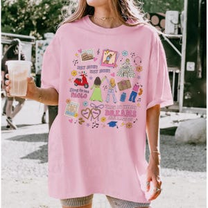 May include: Pale pink t-shirt featuring a vibrant graphic. The design incorporates images of a scooter, the Colosseum, and text that reads "THIS IS WHAT DREAMS ARE MADE OF". The tee has a casual fit and short sleeves, suitable for everyday wear.