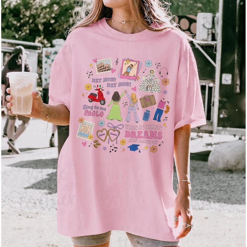 May include: Pale pink t-shirt featuring a vibrant graphic. The design incorporates images of a scooter, the Colosseum, and text that reads "THIS IS WHAT DREAMS ARE MADE OF". The tee has a casual fit and short sleeves, suitable for everyday wear.