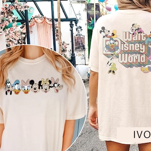 Puede incluir: Dos camisetas de color marfil con diferentes gr&aacute;ficos de Disney World. Una camiseta presenta una l&iacute;nea de personajes cl&aacute;sicos de Disney, incluidos Mickey Mouse, Minnie Mouse, Donald Duck, Goofy y Pluto. La otra camiseta presenta un gr&aacute;fico de estilo retro con el texto "Walt Disney World" y varios personajes de Disney.