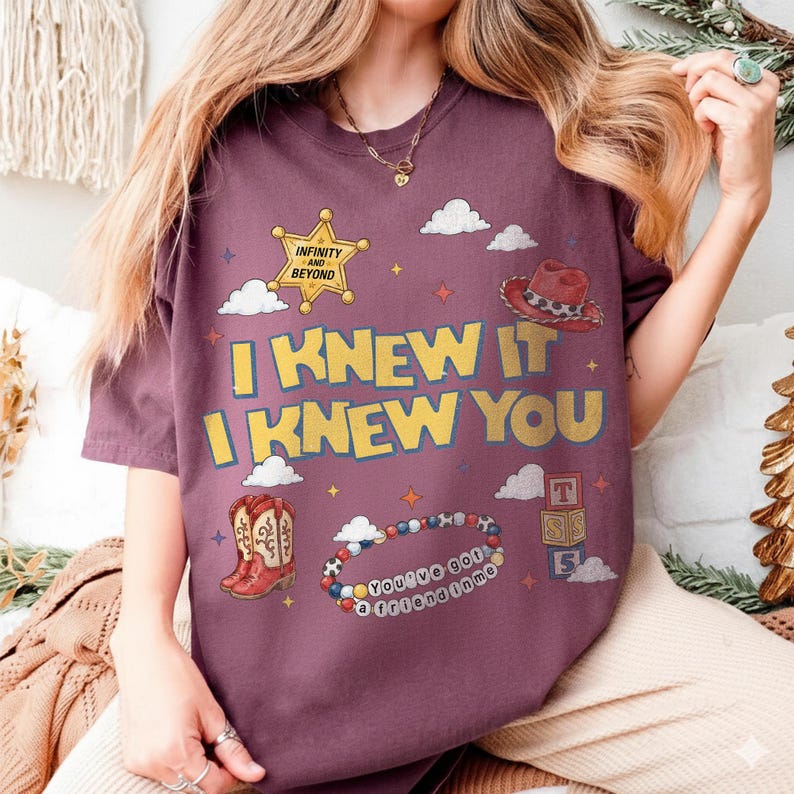 May include: A maroon t-shirt featuring a yellow sheriff star with the text "INFINITY AND BEYOND," a red cowboy hat, a pair of red cowboy boots, a beaded bracelet with the text "YOU'VE GOT A FRIEND IN ME," and the text "I KNEW IT I KNEW YOU."