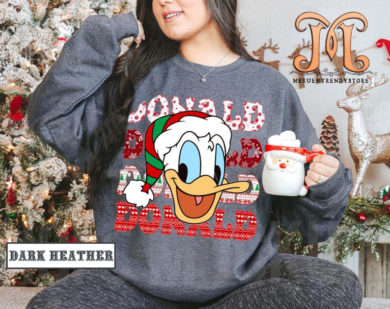 May include: Dark heather gray sweatshirt featuring a Donald Duck graphic wearing a Santa hat. The text "DONALD DAD" is displayed in a festive font. A Santa mug is held in the hand. The words "DARK HEATHER" are at the bottom.