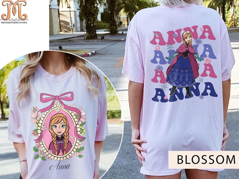 May include: Two pink t-shirts with a Frozen character design. One shirt features a portrait of Anna in a frame with flowers and the text "Anna". The other shirt has the text "Anna" repeated in a retro style with a cartoon image of Anna in a blue and white dress.