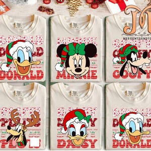 May include: Six cream-colored t-shirts featuring Disney characters in Christmas attire. Donald Duck, Minnie Mouse, Goofy, Pluto, Daisy Duck, and Donald Duck are depicted with festive hats and names in red block letters.