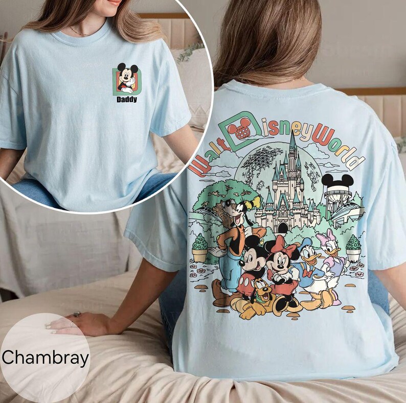 May include: Pale blue t-shirt with a Mickey Mouse graphic and the word "Daddy" on the front. The back of the shirt features a colourful Walt Disney World design with cartoon characters and the park's name.