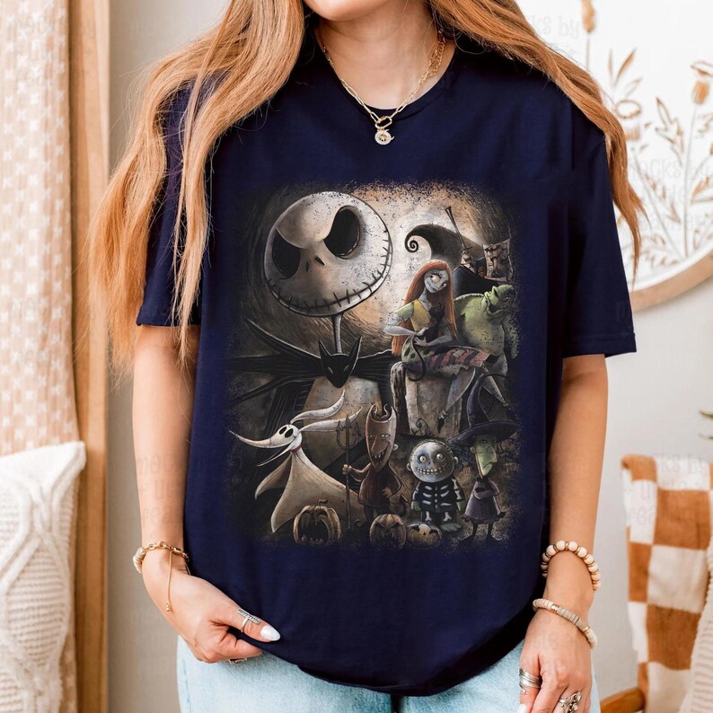 May include: Navy blue t-shirt featuring a graphic of characters from The Nightmare Before Christmas. The design includes Jack Skellington, Sally, Zero, and other characters in a spooky, Halloween-themed illustration.