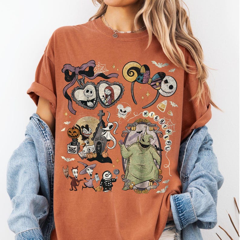 May include: A rust-colored t-shirt featuring a graphic print of characters and icons from The Nightmare Before Christmas, including Jack Skellington, Sally, Zero, and Oogie Boogie, arranged in a collage with bows, bats, and text elements.