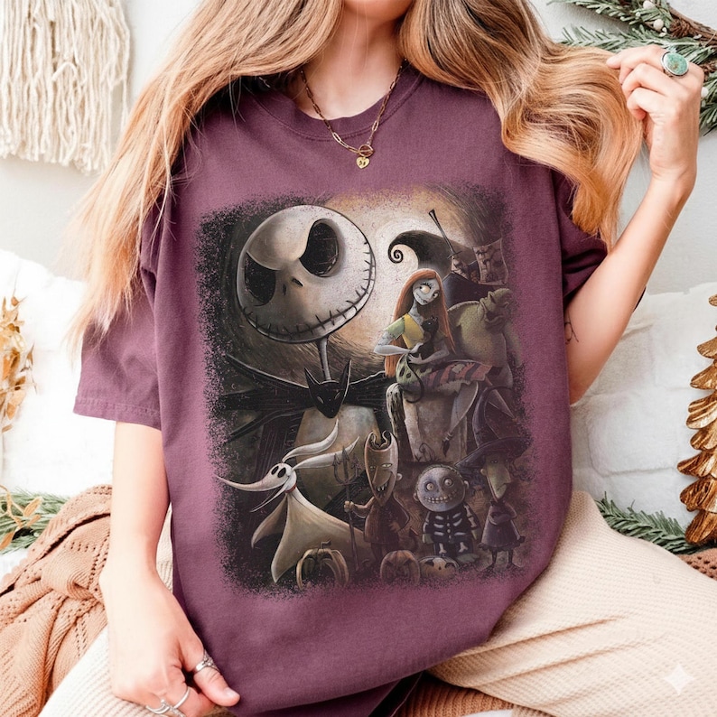 May include: A maroon t-shirt featuring a graphic of characters from The Nightmare Before Christmas. The design includes Jack Skellington, Sally, Zero, and other characters in a dark, spooky scene. The shirt is a relaxed fit.