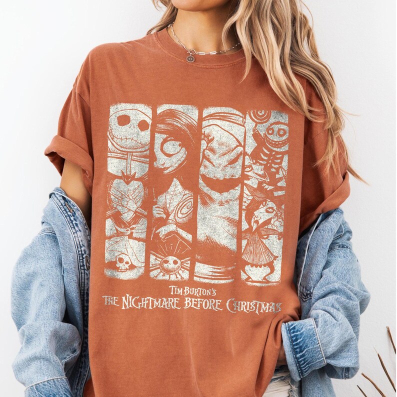 May include: A rust-colored short-sleeve t-shirt featuring a distressed white graphic print of characters from Tim Burton's The Nightmare Before Christmas, including Jack Skellington, Sally, and Oogie Boogie, arranged in four vertical panels.