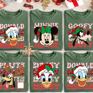 May include: Six green t-shirts featuring Disney characters in Christmas attire. Donald Duck, Minnie Mouse, Goofy, Pluto, and Donald Duck are depicted with festive hats and holiday-themed text. The shirts have a crew neck design.