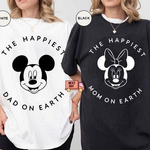 May include: White and black t-shirts with Mickey and Minnie Mouse designs. The white shirt says "The Happiest Dad on Earth" and the black shirt says "The Happiest Mom on Earth". Both shirts have a circular design.