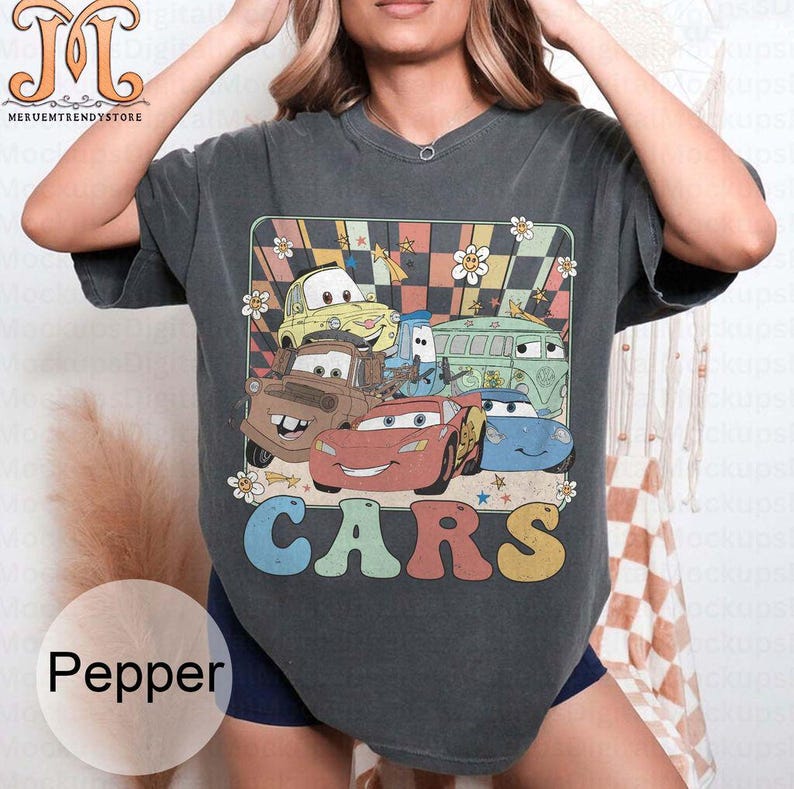 May include: A dark gray t-shirt with a retro-style graphic of cartoon cars from the movie Cars. The graphic features a checkered background with stars and flowers. The text "CARS" is printed in rainbow colors below the graphic.
