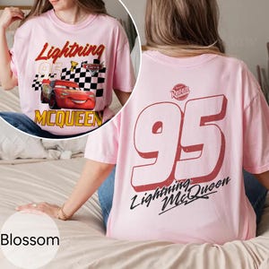 May include: Pink t-shirt featuring Lightning McQueen from the Cars movie. The front graphic includes McQueen, the number 95, and a checkered flag. The back of the shirt displays a large number 95 and the words "Lightning McQueen".