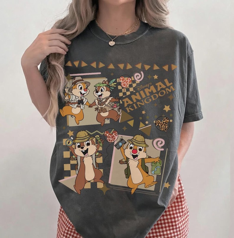 May include: A charcoal gray short-sleeve t-shirt featuring a graphic print of Chip and Dale in safari gear. The design includes the text Disney ANIMAL KINGDOM, along with various geometric shapes, stars, and small animal-print accents.