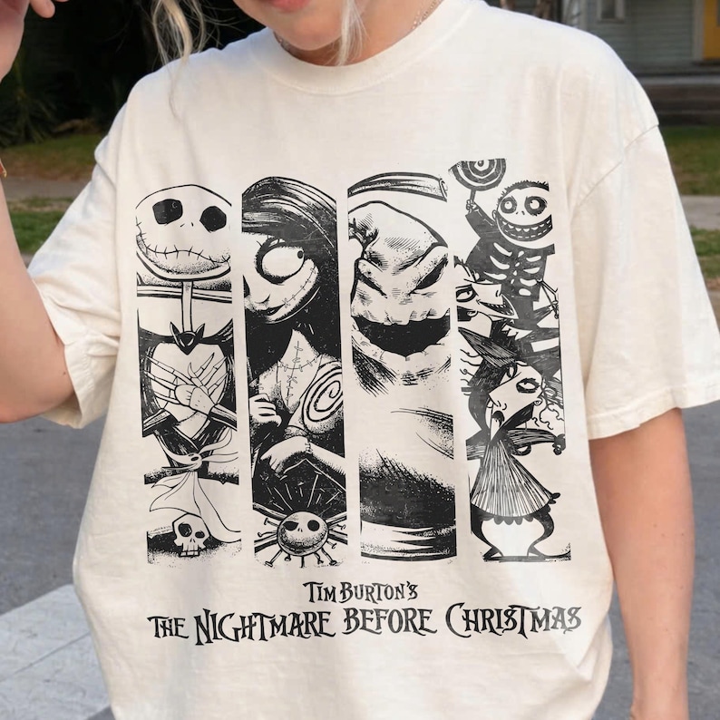 May include: An off-white short-sleeve t-shirt featuring a black graphic print of characters from Tim Burton's The Nightmare Before Christmas. The design includes vertical panels showing Jack Skellington, Sally, Oogie Boogie, and other figures.