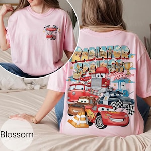 Puede incluir: Camiseta rosa claro con un gr&aacute;fico colorido de personajes de Cars y la inscripci&oacute;n "Radiator Springs" en la espalda. La parte delantera tiene un gr&aacute;fico m&aacute;s peque&ntilde;o con un coche y banderas a cuadros. La palabra "Blossom" est&aacute; en la parte inferior.