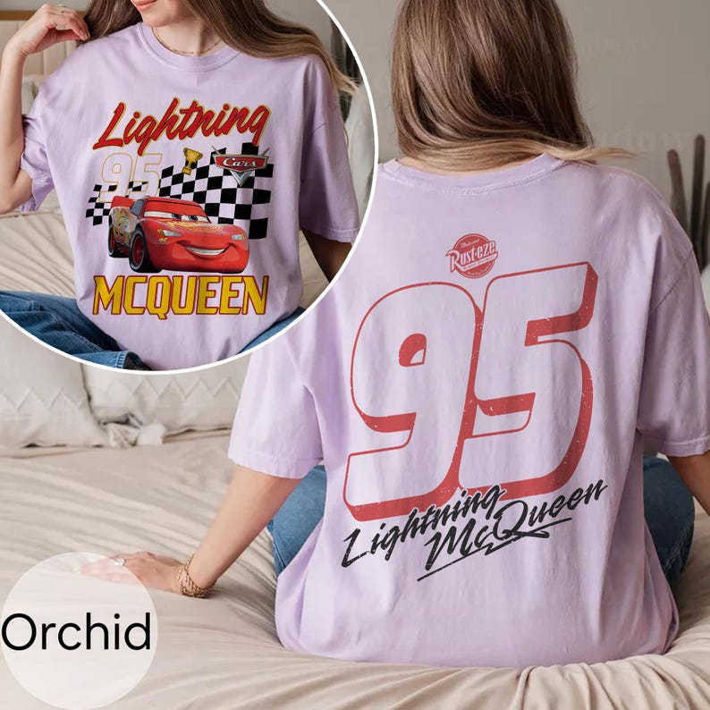 May include: Orchid-colored t-shirt featuring Lightning McQueen from the Cars movie. The front graphic includes the text "Lightning McQueen" and "95" with a checkered flag. The back displays a large "95" and "Lightning McQueen" in red and black.