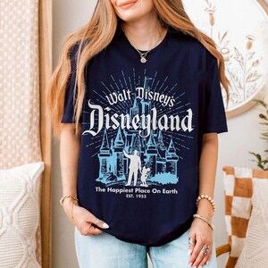 Puede incluir: Camiseta azul marino con un gr&aacute;fico azul claro de Disneyland. El dise&ntilde;o incluye el texto "Walt Disney's Disneyland", "The Happiest Place On Earth EST. 1955", un castillo y siluetas de una persona y Mickey Mouse.