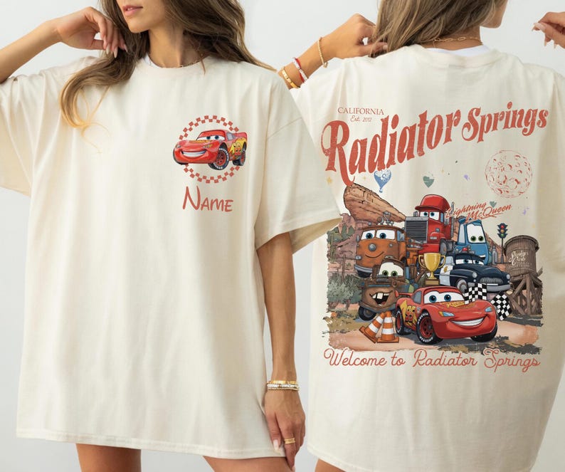 Op de afbeelding: Cr&egrave;mekleurig T-shirt met een rode raceauto-afbeelding en de naam "Name". De achterkant van het shirt heeft een vintage ontwerp met de tekst "Radiator Springs" en cartoon-autokarakters.