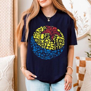 May include: Navy blue t-shirt featuring a colorful graphic of a ball composed of various character silhouettes. The ball design includes red, yellow, and blue sections. The shirt is a casual wear item.