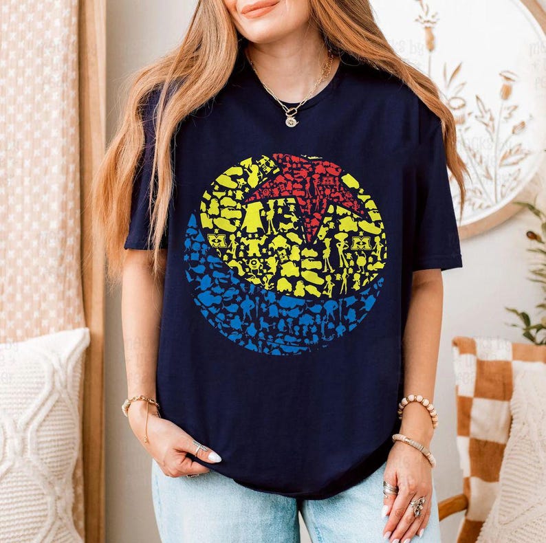 May include: Navy blue t-shirt featuring a colorful graphic of a ball composed of various character silhouettes. The ball design includes red, yellow, and blue sections. The shirt is a casual wear item.