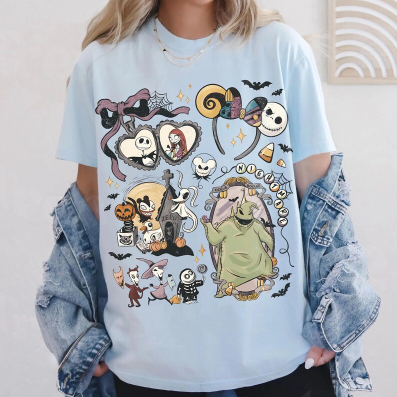 May include: A light blue t-shirt featuring a graphic print of characters and icons from The Nightmare Before Christmas, including Jack Skellington, Sally, Oogie Boogie, Zero, and Lock, Shock, and Barrel, arranged in a collage with bats and stars.