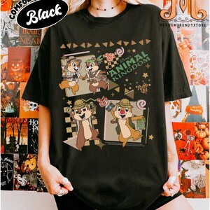 May include: A black short-sleeve t-shirt featuring a graphic print of Chip and Dale in explorer outfits. The design includes the text Disney's ANIMAL KINGDOM, along with various geometric shapes, stars, and small icons of animal-print ears.