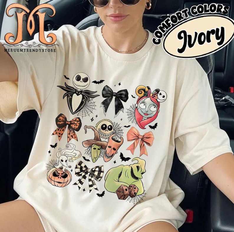 Puede incluir: Camiseta de color marfil con personajes tem&aacute;ticos de Halloween y dise&ntilde;os de lazos. El gr&aacute;fico incluye a Jack Skellington, Sally, Oogie Boogie y otros personajes de The Nightmare Before Christmas. La camiseta tambi&eacute;n tiene el texto "COMFORT COLORS" e "Ivory".
